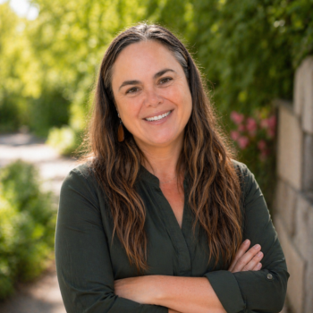Professional headshot of women smiling with arms crossed, outdoors against a green leafy background.